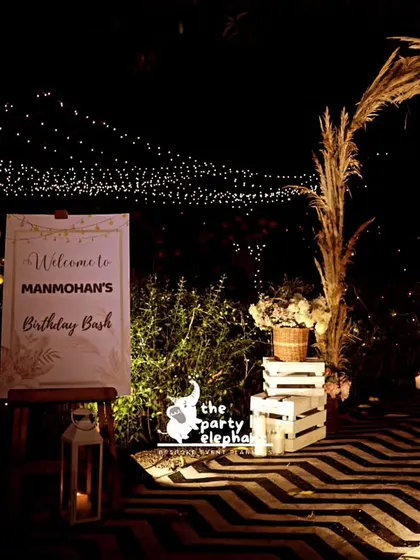 The welcome area for the black and gold party featured a personalized sign on an easel, a lantern with a candle, and the stunning pampas grass archway, all set against a stylish chevron-patterned floor.