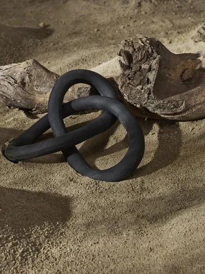 A black sculptural object placed on sand and driftwood. This image treats the decor piece like a found object of art, giving it a sense of history and intrigue.
