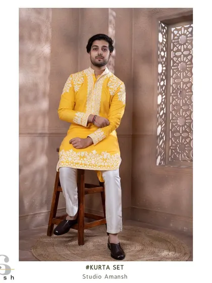 A seated full-length shot of the zesty yellow kurta, paired with white trousers and classic shoes.