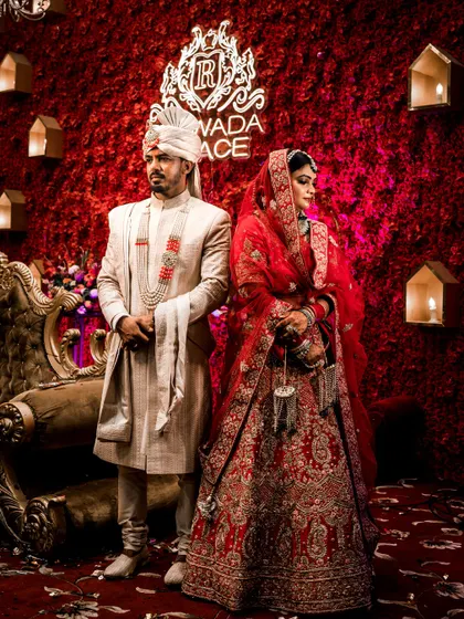 A royal portrait of the bride and groom against a rich, red floral wall with their wedding logo.