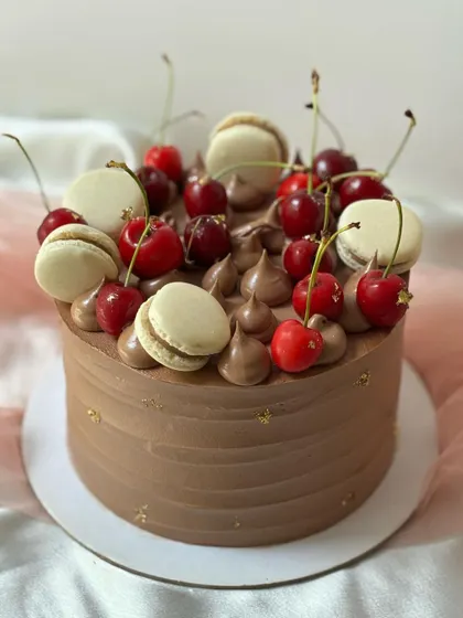 A rich chocolate buttercream cake topped with fresh cherries and macarons. The gold dust adds a little sparkle to this indulgent treat.