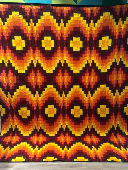 A showcase of bold, modern design. This Bargello quilt uses a special piecing technique to create a sense of movement and depth with its vibrant, fiery colors, demonstrating our skill in contemporary quilt patterns.