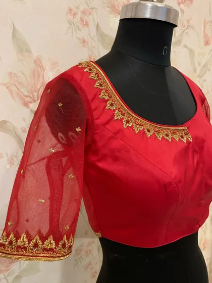 A classic red blouse with sheer net sleeves, featuring simple gold embroidery on the neckline and cuffs.
