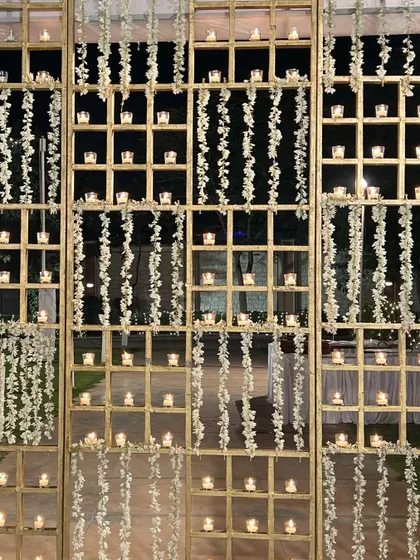 A wall of candles set in a golden grid, with hanging floral strings, adding a touch of traditional opulence to the decor.