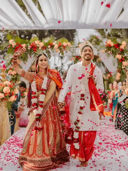 A joyous moment captured as the couple walks down the aisle after their wedding ceremony. The pathway is lined with flower petals, and the background shows the elegant floral arch and draped canopy of the mandap we designed.