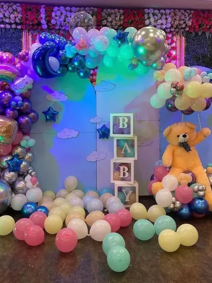 A whimsical 'BABY' themed decoration with a large teddy bear, 'BABY' boxes, and a rainbow-lit balloon arrangement.