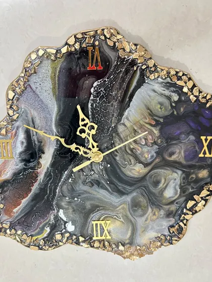A dark, dramatic geode-style clock with swirls of black, white, and purple, edged with gold-colored stones.