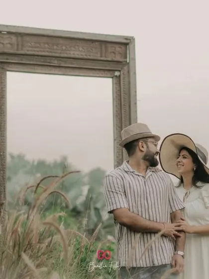 A creative pre-wedding shot using a large, empty frame in a field of tall grass. This setup adds an artistic and surreal touch to the couple's portraits.