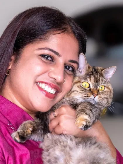 A smiling pet parent holding her beloved cat. The genuine joy and comfort of being at home is evident in this photo.
