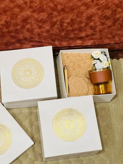 An open and closed view of a corporate gift box. The elegant white box with a gold mandala design opens to reveal a curated set of high quality office accessories.