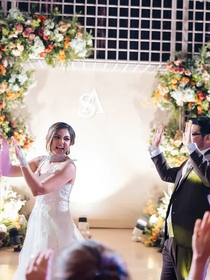 The dance floor is alive with energy. The couple and their guests celebrate in front of a stage framed by beautiful, lush floral arches.