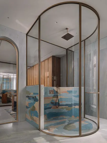 The centerpiece of the master bathroom is this cylindrical shower cubicle, framed in brass, with a floor-to-ceiling mosaic that feels like a watercolor painting.