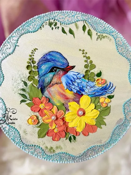 A 10-inch circular wall plate featuring a colorful painted bird surrounded by sculpted orange and yellow flowers.