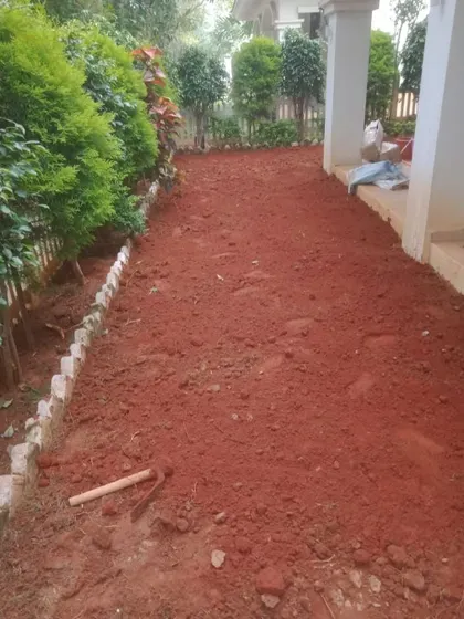This area has been prepared with red soil and a stone border, ready for the installation of shade grass.