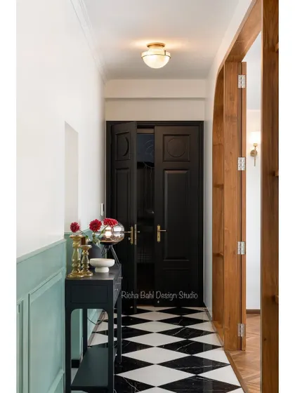 The entryway of the young couple's Mumbai home. The classic black and white marble floor, paneled walls, and a simple black console create an entrance that is elegant, timeless, and welcoming.