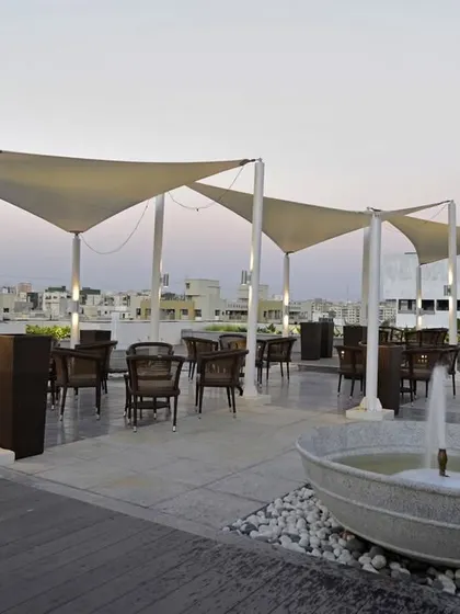 A rooftop coffee lounge with tensile fabric canopies for shade. The space includes comfortable seating and a small water feature, creating an urban oasis.
