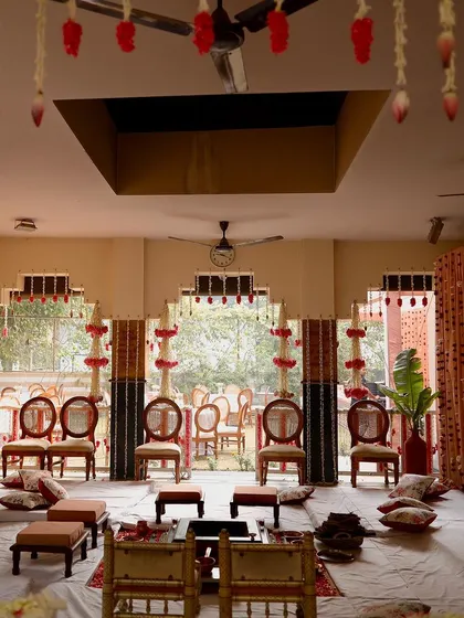 The main ceremony area for a traditional wedding, featuring low seating (bajots) and chairs arranged under a canopy of hanging floral decorations. The design is both traditional and elegant.