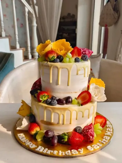 A fresh and vibrant two-tier fruit drip cake, adorned with strawberries, blueberries, grapes, and yellow sugar flowers.