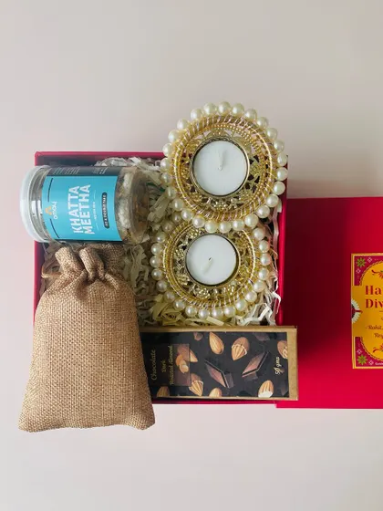 A simple and sweet Diwali gift box, containing a jar of khatta meetha, a chocolate bar, a jute potli, and two pearl diyas.