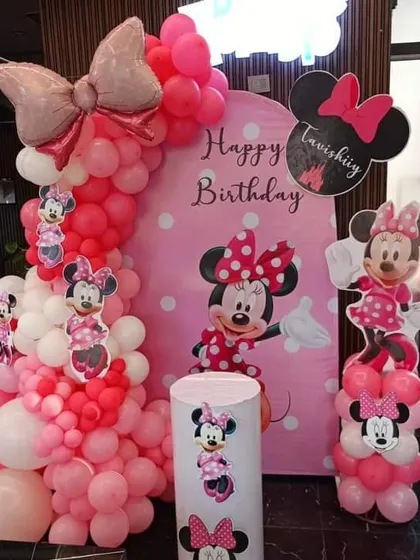 A classic Minnie Mouse theme for a birthday party. This decoration features a pink and red balloon arch, a Minnie Mouse backdrop, and character cutouts.
