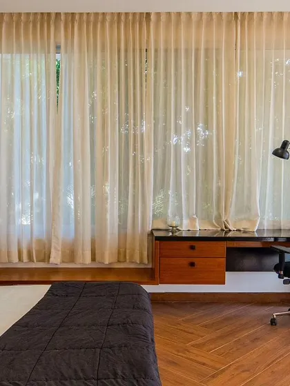 A minimalist home office setup within a bedroom, featuring a floating wooden desk placed against a large window with sheer curtains, creating a bright and inspiring workspace.