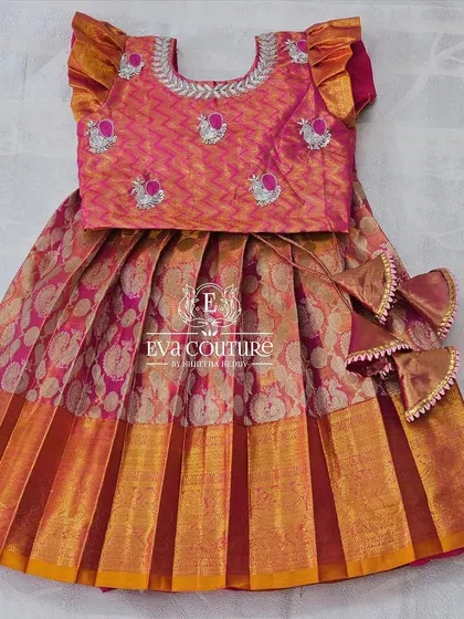A sweet pattu lehenga for a 6-month-old. The pink blouse has delicate embroidery, and it's paired with a pink and orange brocade skirt.
