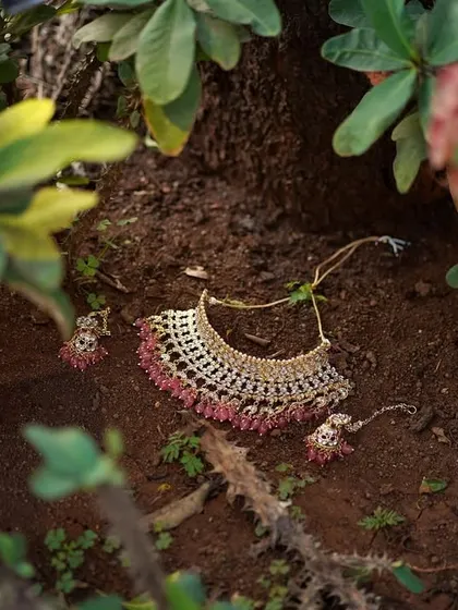 A creative shot of the bride's necklace and earrings, laid out on the ground amidst nature. This photo highlights the beauty of the bridal jewelry.