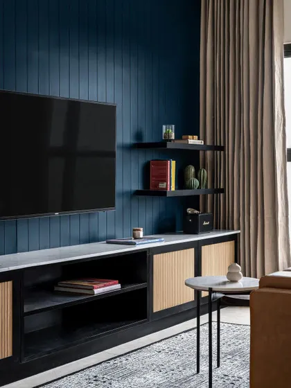 The moody lounge space in a modern compact home. A deep blue paneled wall serves as the backdrop for the TV, while the fluted detail on the console adds texture.