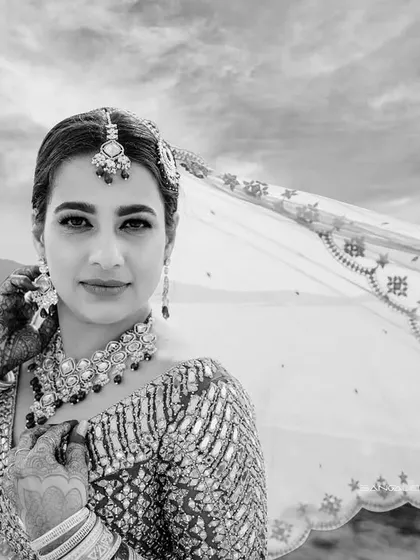 A classic black and white bridal portrait from a pre-wedding shoot. The wind catching her veil against the sea creates a timeless and dramatic effect.