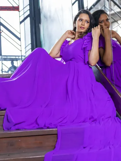 A model sitting on a staircase in the flowing purple gown, with the reflection creating a beautiful visual effect.