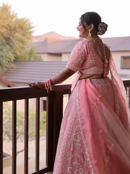 Blushed pink dreams. This bride looks out from her balcony, her soft pink lehenga and romantic makeup creating a truly dreamy and picturesque moment.