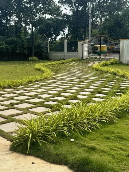 A wide walkway made of square stone pavers with grass growing in the gaps, bordered by ornamental grasses. This design blends hardscaping with softscaping for a softer, greener look.
