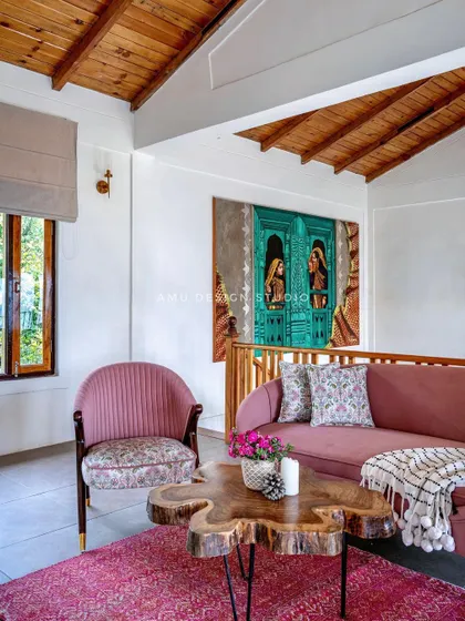 The upper lounge area in 'The Mountain Home,' featuring a custom pink sofa, a live-edge coffee table, and a large, vibrant painting that adds a splash of color to the rustic-chic space.