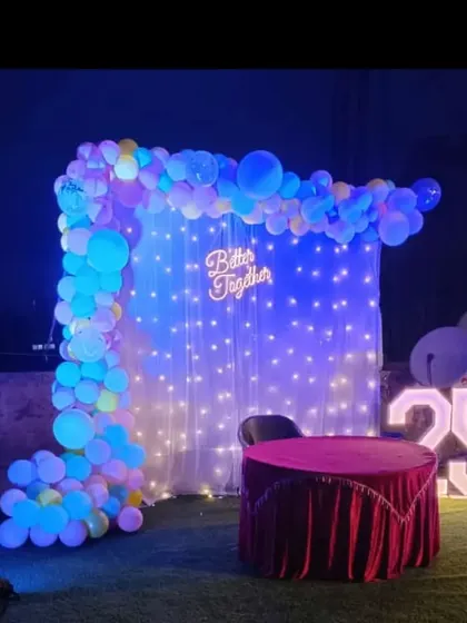 A terrace party setup for a 25th birthday, featuring a balloon arch, fairy light curtain, and marquee numbers.