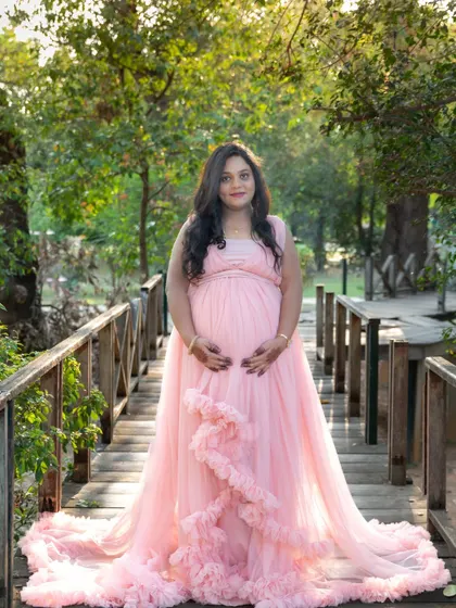 A lovely portrait of a mom-to-be in a pink gown, standing on a wooden bridge in a park.