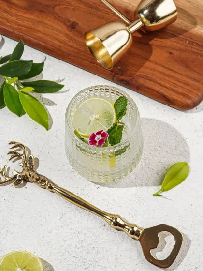 A minimalist product shot of a deer-head bottle opener and other bar accessories, styled with fresh lime and mint for a refreshing summer feel.