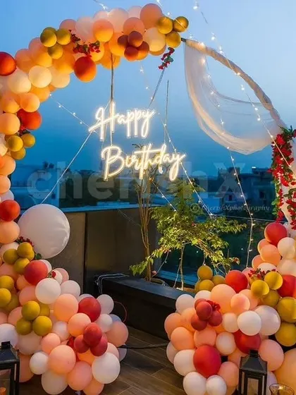 A stunning sunset-themed terrace decoration. This circular balloon arch uses shades of orange, yellow, and red, with a neon sign and fairy lights.
