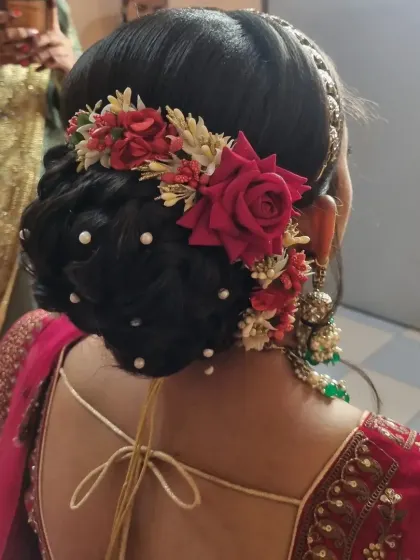 This bridal look features a beautiful red and green color combination. The hairstyle is a classic bun decorated with red roses and pearls, complementing her stunning lehenga.