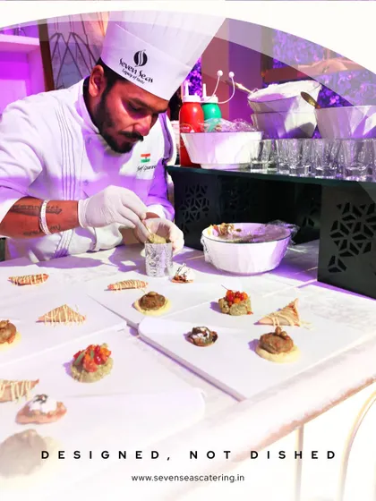 "Designed, Not Dished." A chef carefully assembles a variety of canapés. This tagline encapsulates our philosophy of treating every dish as a design piece, crafted with intention and artistry.