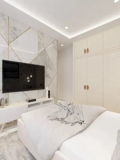 In this bedroom, I designed a feature wall with white marble-finish panels and gold inlay for the TV area. The clean, handleless wardrobes provide ample storage while maintaining a minimalist and spacious look.