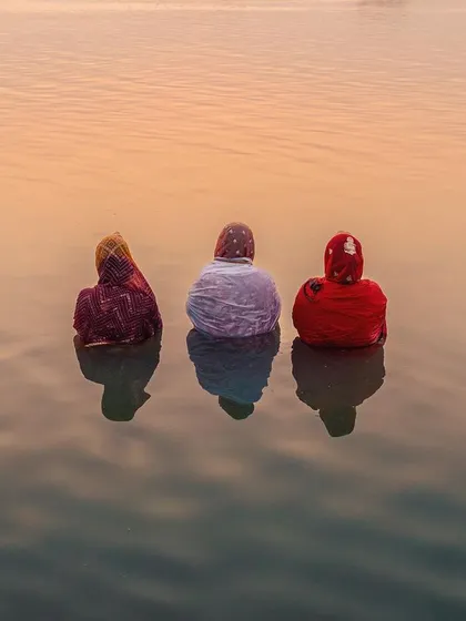 Three women offer prayers during Chhath Mahaparv in Bihar, their forms reflected in the calm water at dusk. This image captures the quiet, painterly beauty of faith, a moment of pure tranquility and devotion.