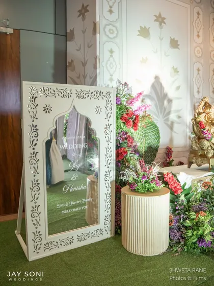 Personal touches make an entrance special. For this wedding, I placed a beautiful welcome mirror with intricate jaali-work details amidst a garden of colorful flowers, offering a warm and personalized greeting.