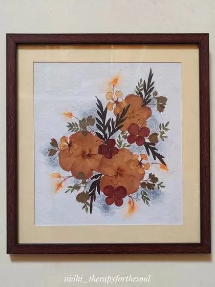 A framed piece of pressed flower art hanging on a wall. The simple wooden frame and matting give it a classic, elegant look.