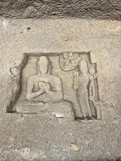 A small, detailed rock carving inside Kanheri Caves depicting a meditating Buddha figure.