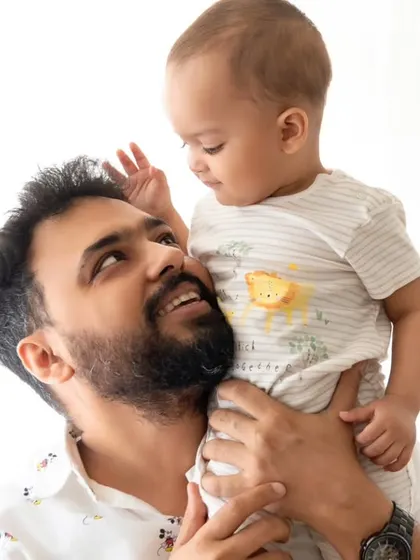 A father looks up at his son, whom he is holding on his shoulders, sharing a sweet, interactive moment.