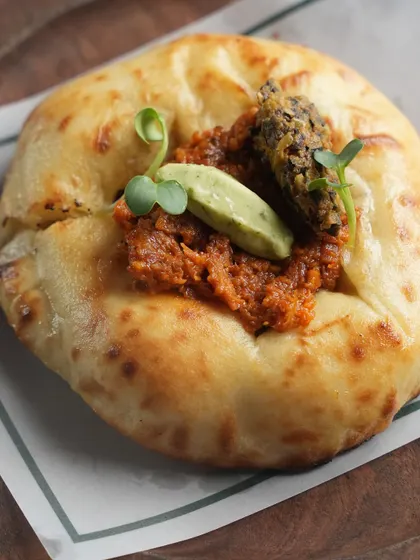 Our Pulled Duck Kulchette, a small, fluffy bread topped with tender pulled duck, herb butter, and a tangy tapenade pickle. A sophisticated and flavourful bite.