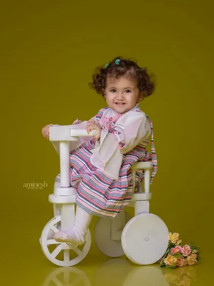 A simple and classic portrait of a little girl on a white tricycle. The solid green-yellow background makes her striped dress and happy face the center of attention.
