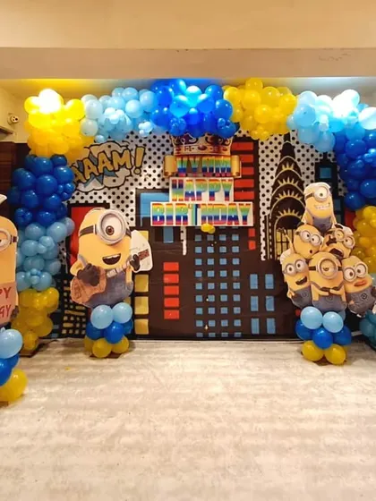 An elaborate Minions birthday party decoration with a city skyline backdrop and multiple character cutouts, creating an immersive themed experience.