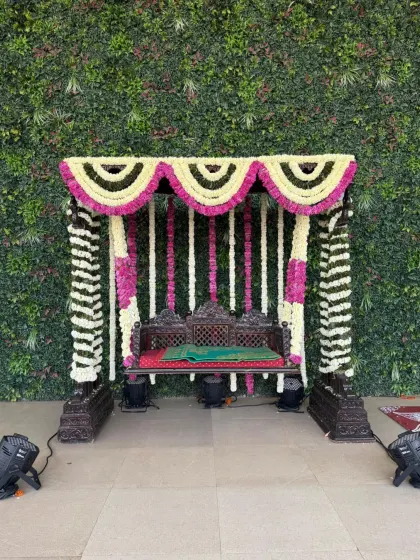 A traditional floral jhula, or swing, beautifully decorated with white and pink flowers. Set against a lush green wall, this swing becomes a perfect spot for photos and rituals during wedding festivities.