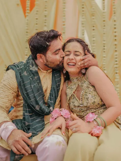 A tender moment as the groom gives his bride a sweet kiss on the cheek during their fun-filled Haldi ceremony.